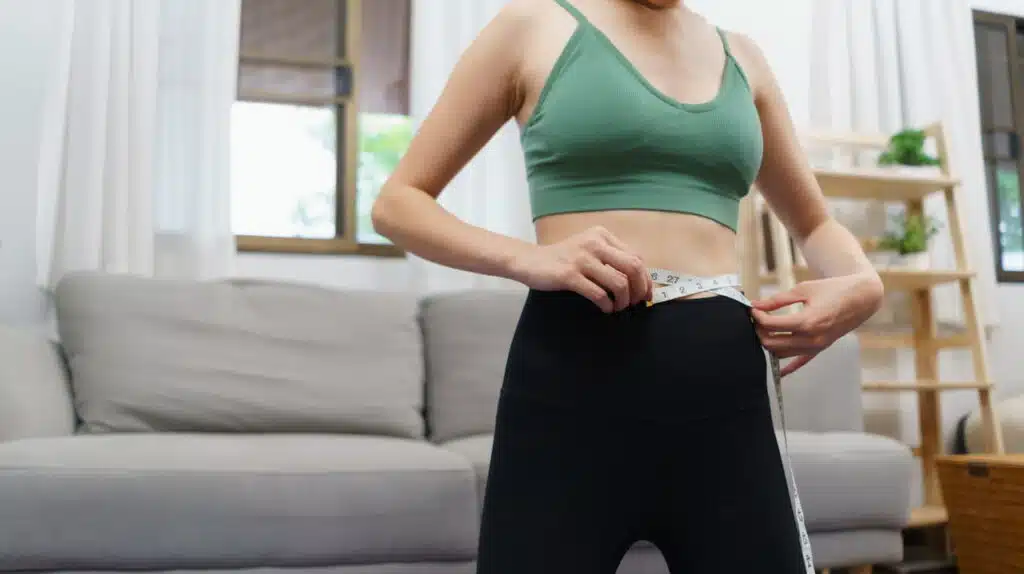 Woman measuring her waist using tape measure.