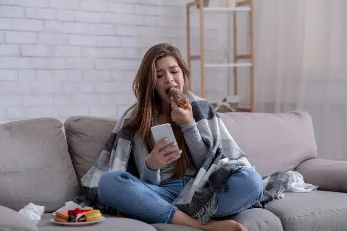 upset woman emotional eating a doughnut on the couch