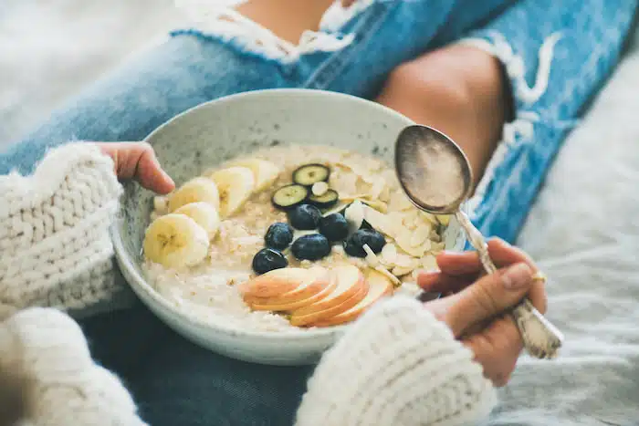 woman in jeans eating healthy oatmeal bowl with fruits to combat emotional eating